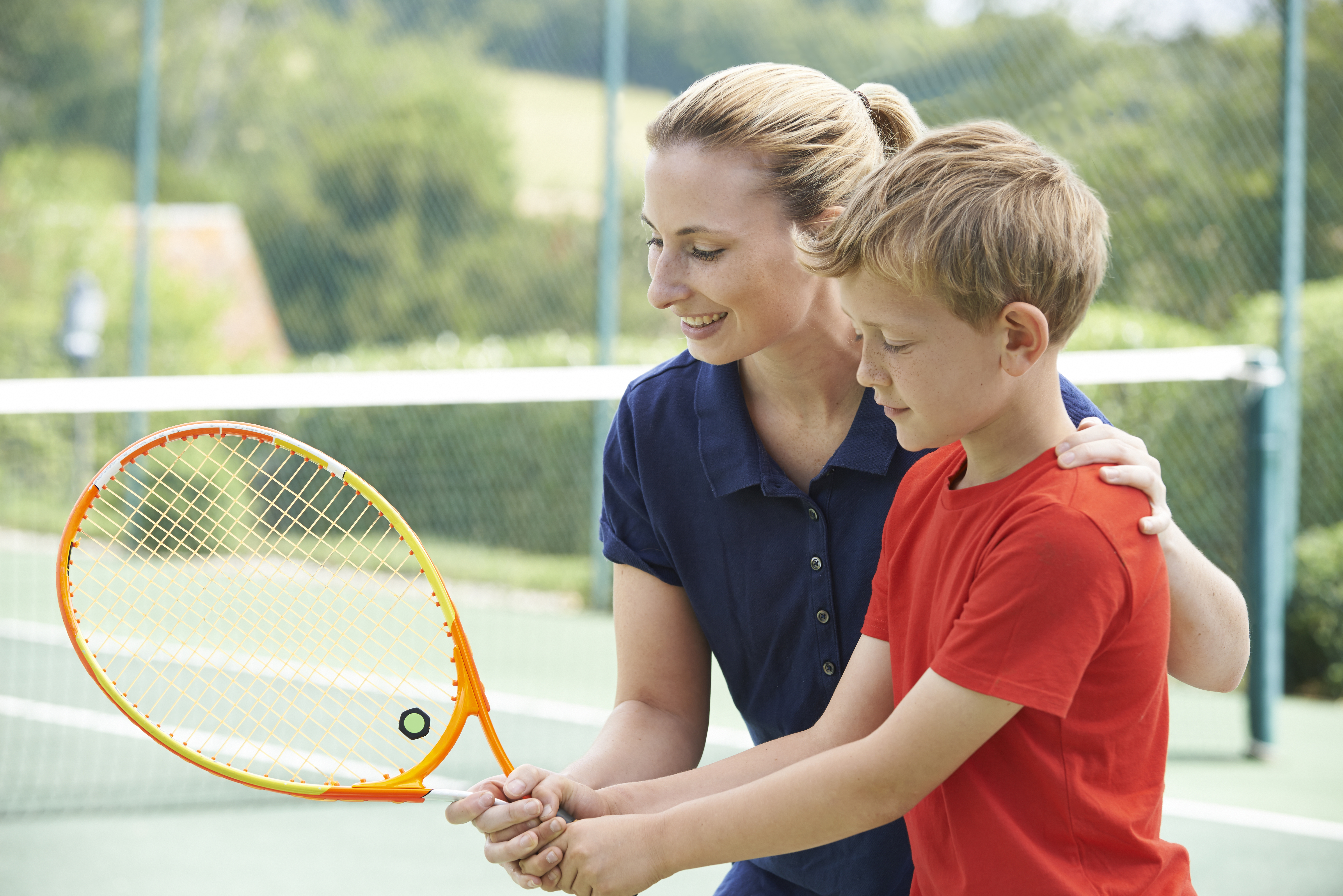 Female Tennis Coach Giving Lesson To Boy